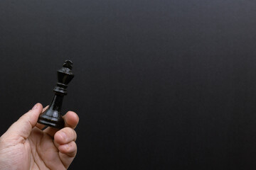 Hand holding a chess queen against a black background