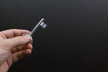 Hand holding a silver key against a black background. Symbolizing opportunity, freedom, access, potential, solution.