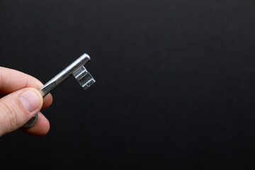 Hand holding a silver key against a black background. Symbolizing opportunity, freedom, access, potential, solution.