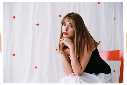 Sad oman poses in a black outfit against a backdrop whit red hearts