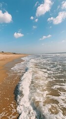 Serene beach scene Waves gently lapping on a sandy shore under a vibrant blue sky dotted with fluffy white clouds. Perfect for travel or summer themes.
