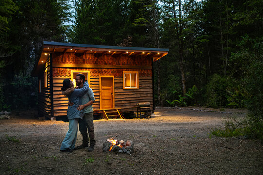 romantic Couple by a Campfire in Front of a Rustic Cabin in the Woods