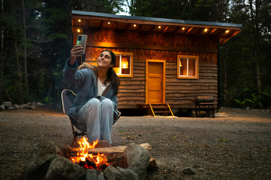 woman Enjoying a Campfire in Front of a Rustic Cabin in the Woods