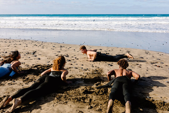 Diverse group of friends practicing surfing techniques on the sand