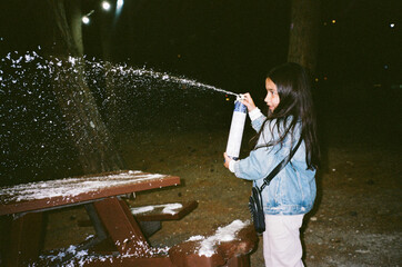 Girl spraying artificial snow into the air at night
