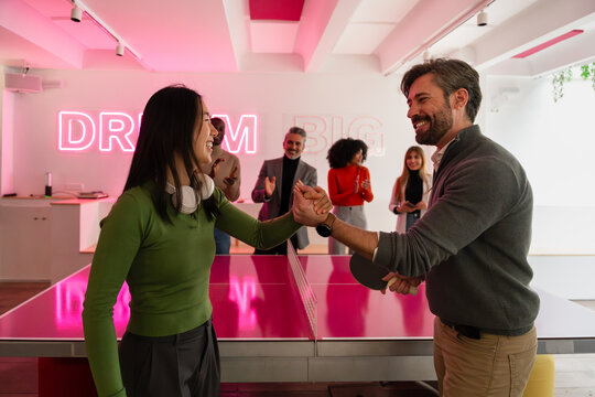 Pink-themed office ping pong match with coworkers cheering
