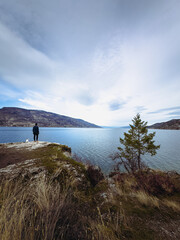 man with dog standing on the edge of a cliff admiring the lake and mountain views