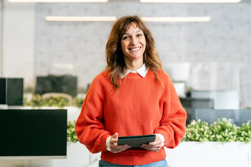 Smiling businesswoman holding tablet and standing in modern office