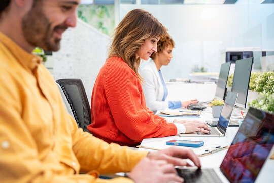 Office workers typing on laptops, working together in modern office