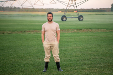 Fototapeta premium Farmer standing in a grassy field. A man harvesting vegetables on a farm. A farmer using irrigation on a farm. A man working in a green field. American farmer inspecting a harvest-ready field.