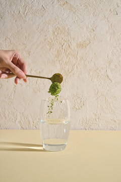 Hand Pouring Matcha Powder Into a Glass of Water