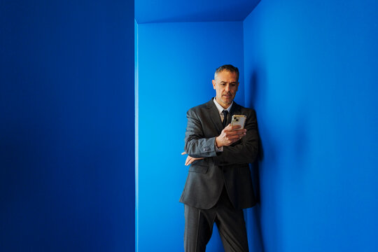 Confident formal businessman using smartphone in blue corner