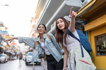 Two Asian young woman waving hand, calling taxi on road in city street. 
