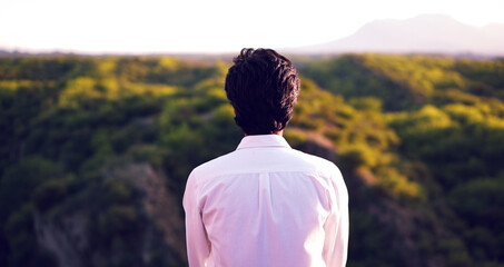 Person in a white shirt faces away while gazing at a lush green valley and distant mountains under...