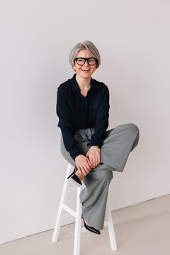Mature woman with gray hair sits confidently on a stool