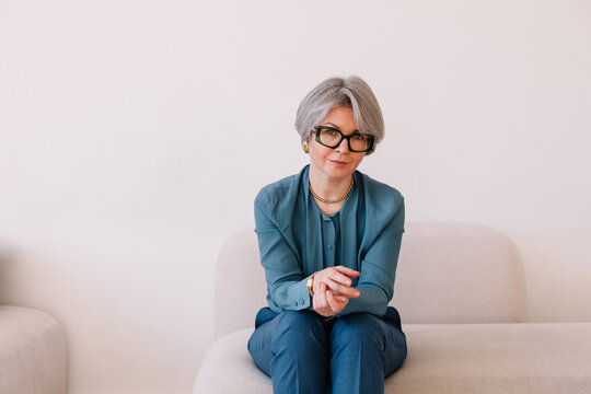 Stylish woman with gray hair seated on a light-colored couch
