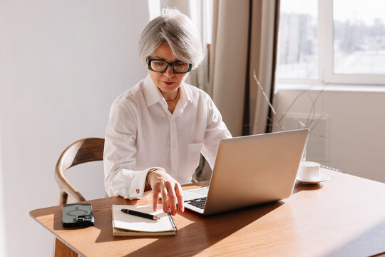Senior woman working on laptop at home during the day with notepad