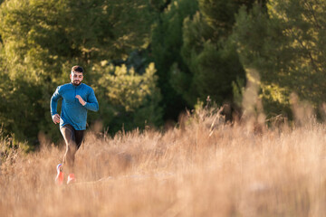 Young male athlete running in a field of dry grass near a forest