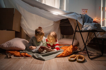 Children watching smartphone inside a blanket fort in bedroom
