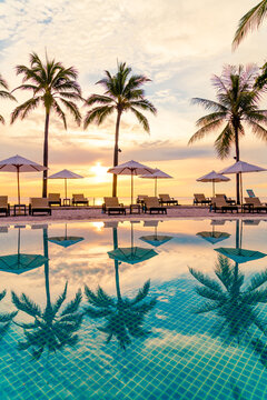 Umbrella and chair around swimming pool in hotel resort with sunrise in morning
