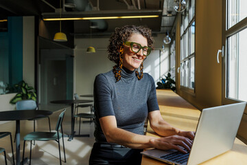 Smiling woman working on laptop in modern coworking