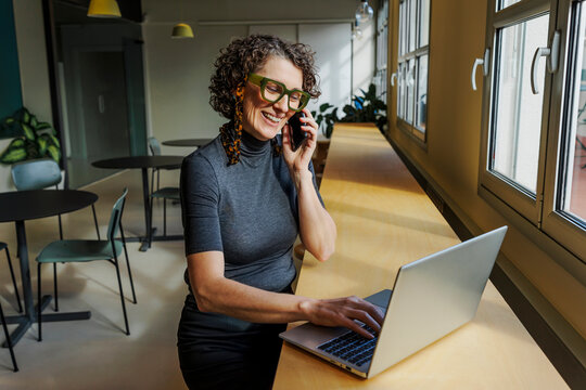Formal businesswoman working on laptop and talking on phone in office - Powered by Adobe