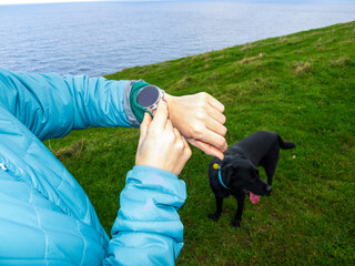 Hiker using smartwatch during trekking excursion with dog by the sea