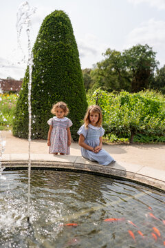 Sisters observing flower and red fish in the gardens of a castle.