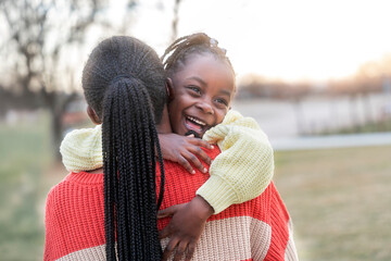 Two happy african sisters are hugging each other at the park