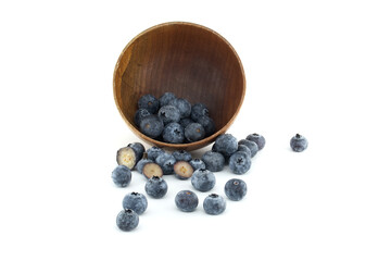 Wooden bowl spills blueberries onto a white surface, highlighting their freshness and natural appeal