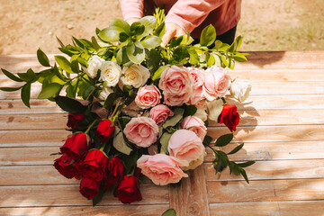 Florist holds a large bouquet of roses against the background of a wooden table. Concept of picking...