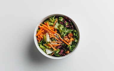 Overhead view of a fresh salad in a white bowl. The salad contains shredded carrots, lettuce, and sesame seeds. The background is white