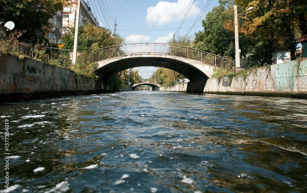 Poster a low-angle view of a waterway with a stone arch bridge in the background. the water is slightly rip