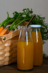 Healthy eating. Two bottles of fresh carrot juice on the table against the background of a wicker basket with carrots.