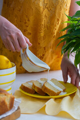 Woman in yellow clothes pouring cream on lemon cake.
