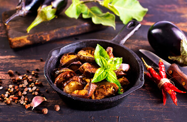 Fried eggplant in a pan. Cooking fried eggplant. Culinary tools, wooden board, knife, fork and spice