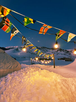 Snowy base camp with yurts, decorated with flags and cozy lights