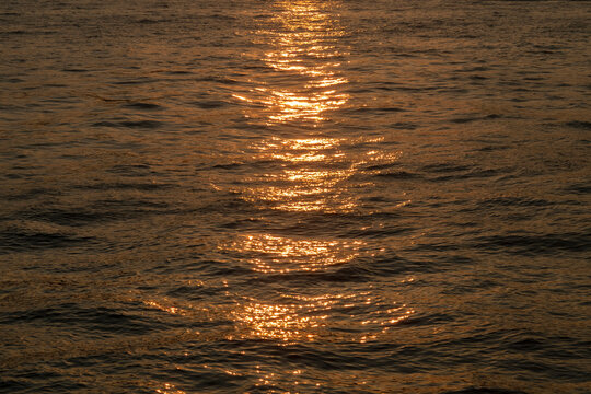 Dark brown rippled sea water surface ans sun reflection