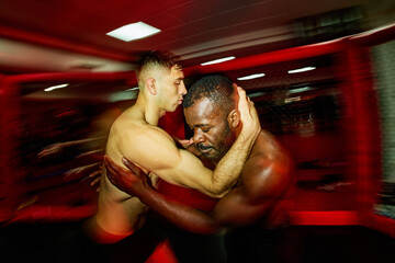 Two athletes engage in a grappling practice in a dimly lit gym