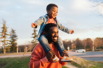 Happy father carrying laughing son on shoulders at park