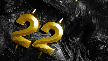 Number 22 golden celebration birthday candle on Black Feathers Background. Twenty-second year....