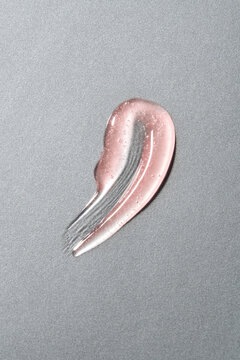 Pink lip gloss swatch smeared on silver background. 