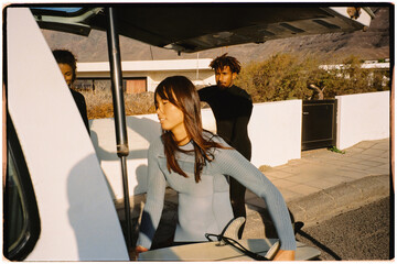 Film shot of asian woman in wetsuit taking a surfboard out of a van