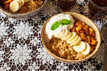 a bowl of caramel apple oatmeal with with banana and yoghurt on lace tablecloths, healthy warm probiotics breakfast
