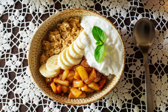 a bowl of caramel apple oatmeal with with banana and yoghurt on lace tablecloths, healthy warm probiotics breakfast