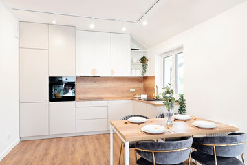 Kitchen interior with white furniture in scandinavian design and dining room with table and chairs. Interior of open space with wooden floor and window in new apartment in luxurious style.