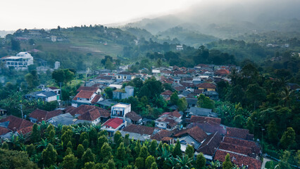 Fototapeta premium An atmospheric aerial image showing a vibrant village surrounded by tropical vegetation and forest, with red-tiled roofs and tight-knit houses