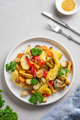 Baked vegetables potatoes, cabbage, pepper and onion in a plate on a light background with fresh parsley.