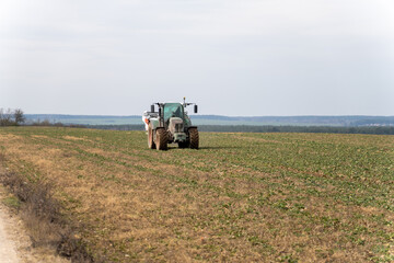 Obraz premium A tractor towing a mineral fertilizer dispenser across a green field