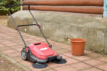 Red outdoor power sweeper rests on a paved surface with black bristles visible, accompanied by an...